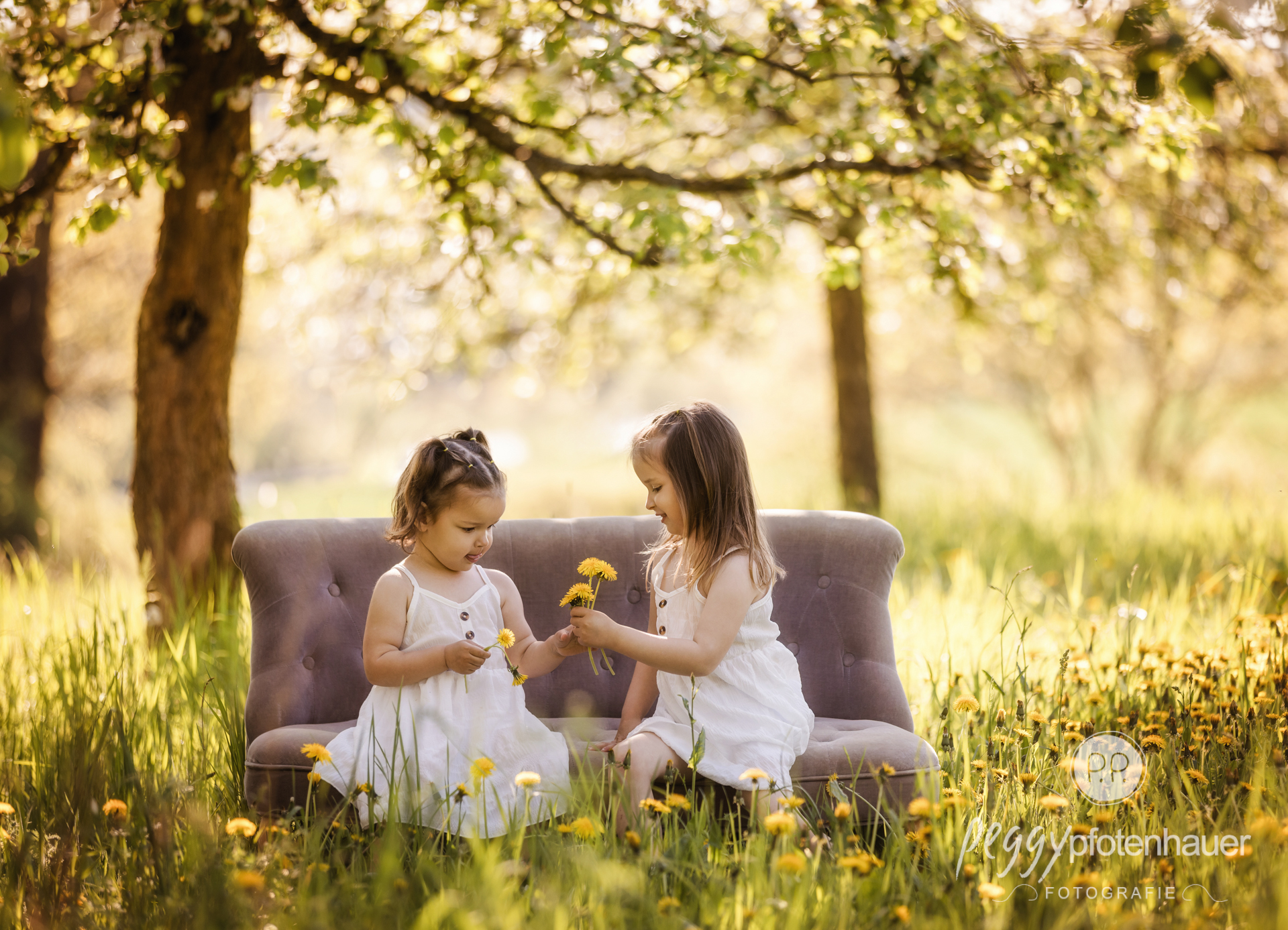 zwei Mädchen sitzen auf Sofa in Wiese und spielen mit Blumen