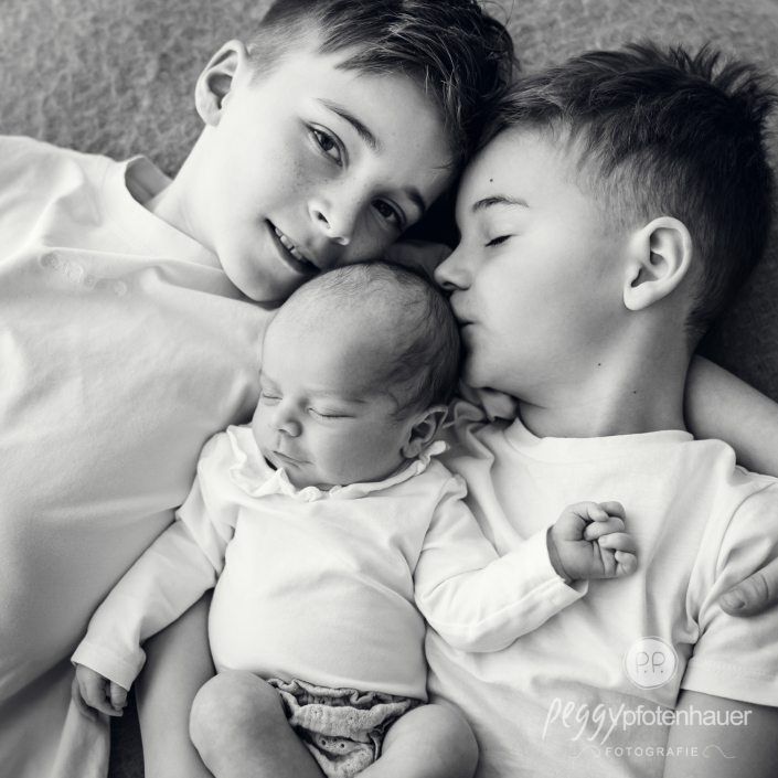 Brüder liegen zusammen mit Baby auf Decke und geben ein Küsschen