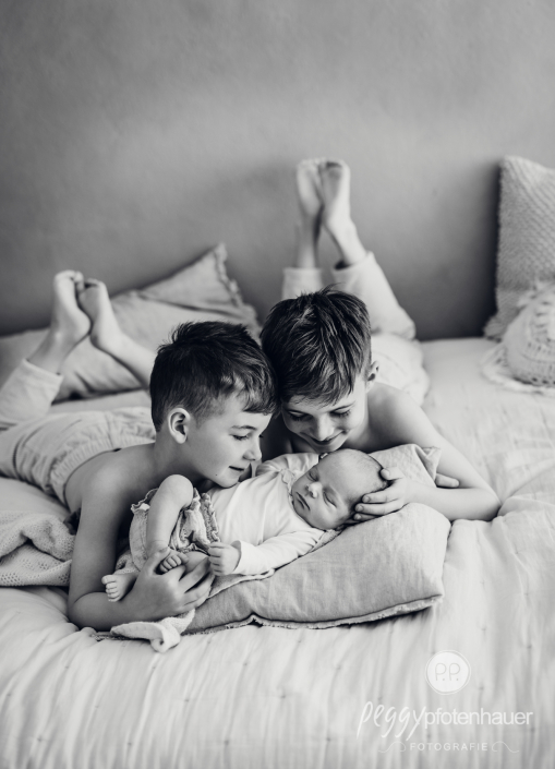 Brüder liegen mit Baby auf Bett und geben ihm ein Küsschen