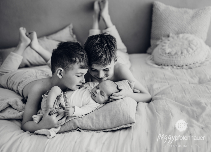 Brüder liegen mit Baby auf Bett und schauen es an