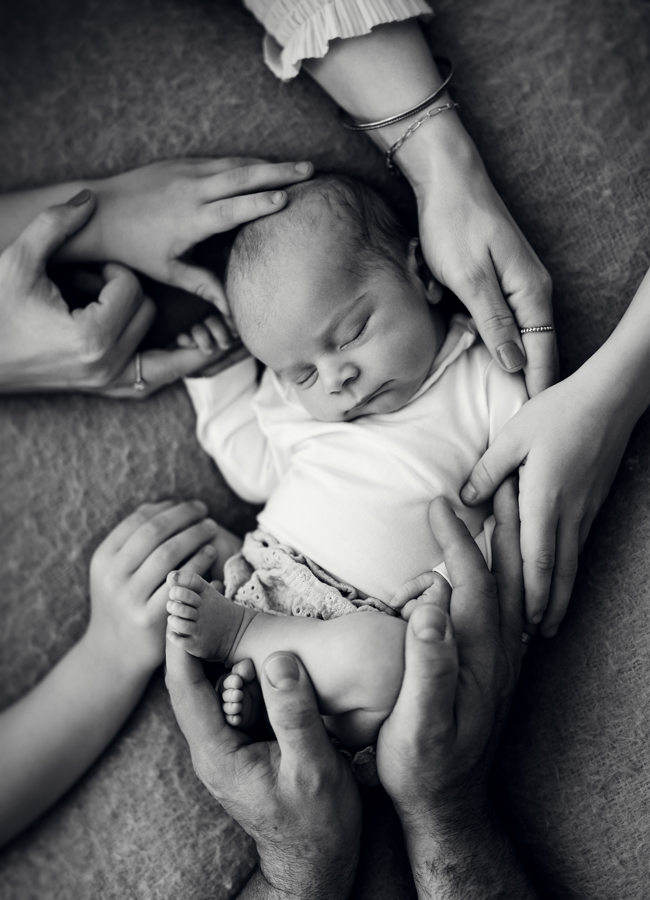 Neugeborenes liegt auf Decke und wird in Händen gehalten
