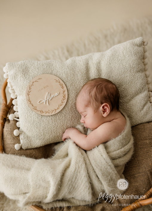 Baby liegt mit Geburtsschild eingekuschelt in Körbchen