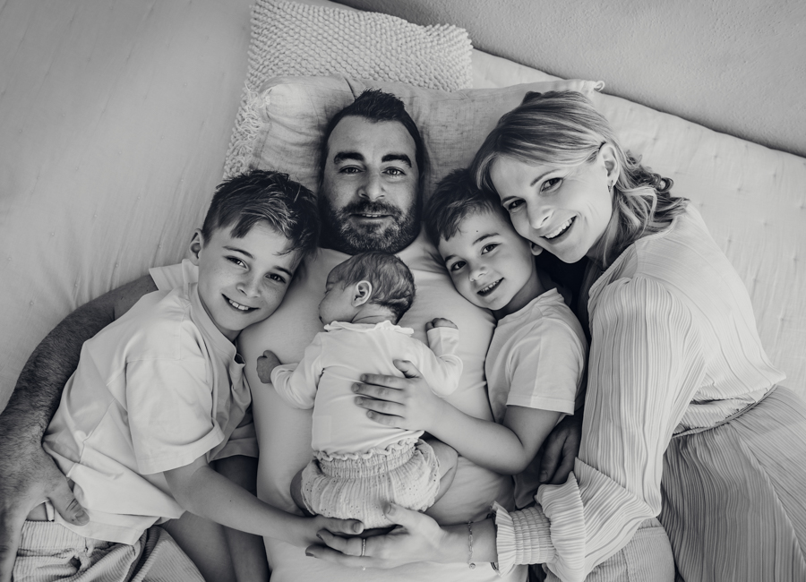 Familie mit drei Kindern liegt auf Bett und lacht