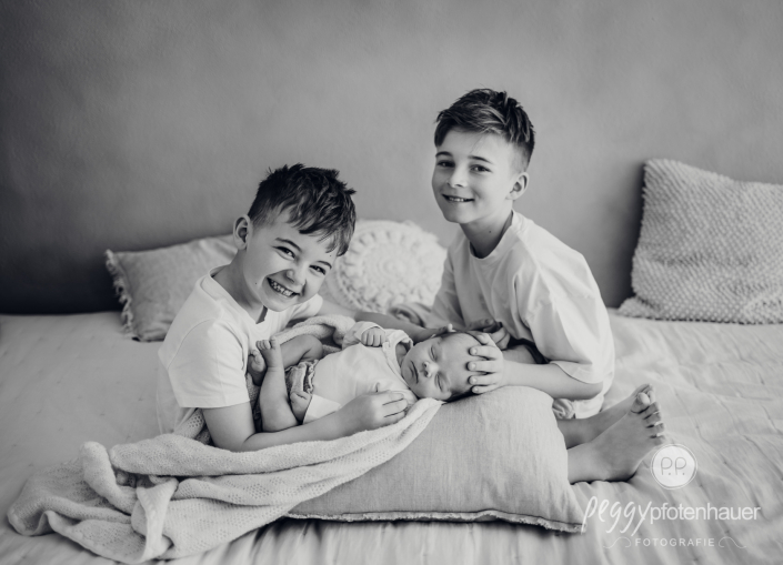 Geschwister haben Baby auf Schoß und sind glücklich