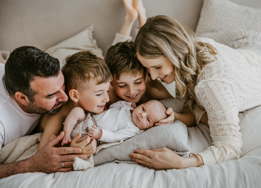 Familie liegt mit Baby auf Bett und schaut es glücklich an