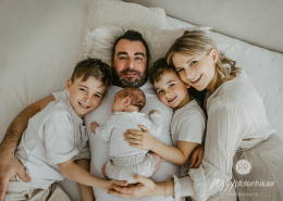 Familie mit Baby liegt auf Bett und ist glücklich