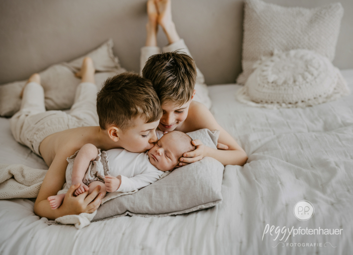 Neugeborenes mit Brüdern auf Bett