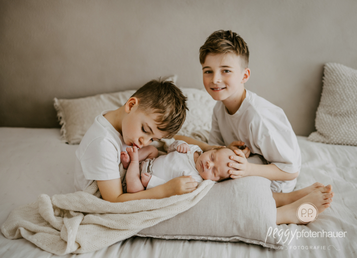 Geschwister halten Baby und kuscheln mit ihm