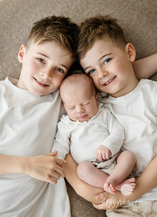 Geschwister mit Baby liegen auf Decke und lachen