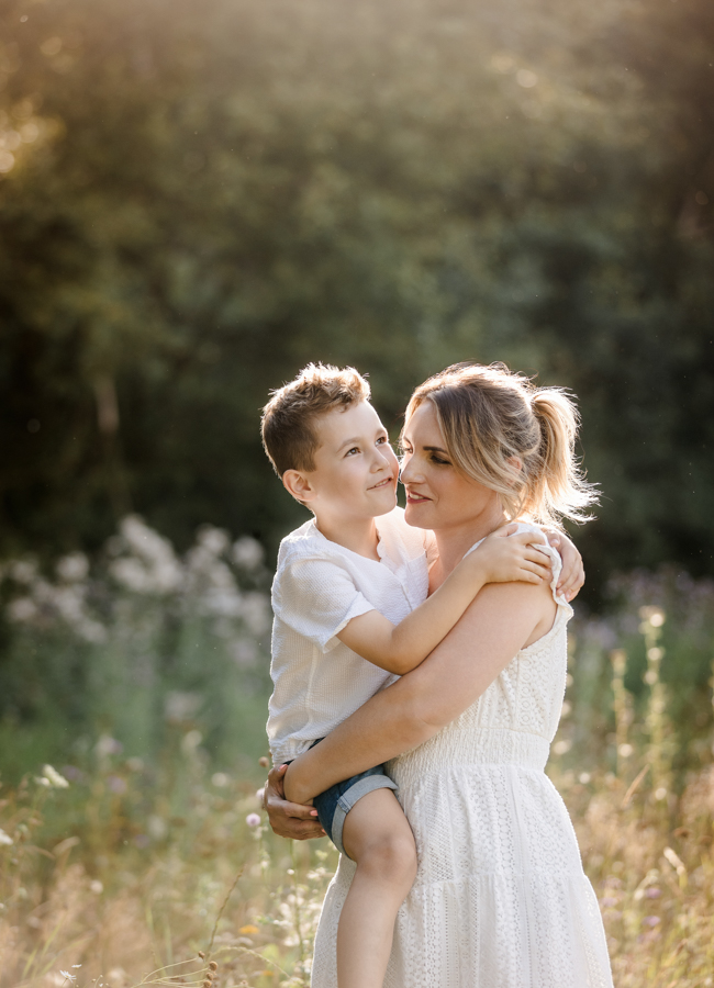 innige-mama-kind-portraits Mama und Sohn laufen gemeinsam durch Wiese im Abendlicht und sind im Moment versunken