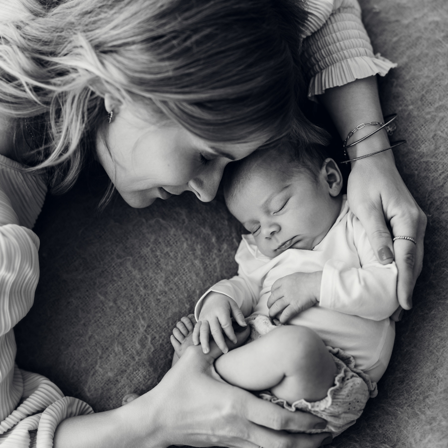 Mama und Baby liegen auf Decke und kuscheln