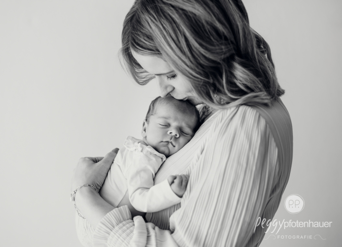 Mama steht mit Baby im Arm und küsst es
