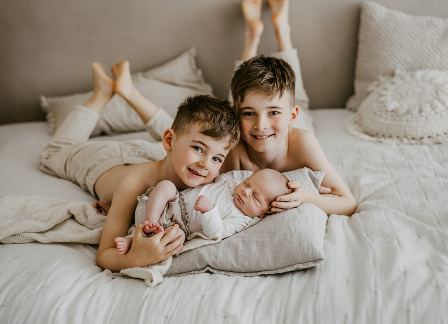 Geschwister liegen mit Baby auf Bett und lachen