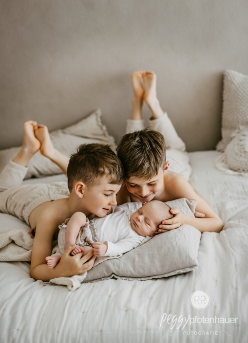 Geschwister kuscheln mit Baby auf Bett
