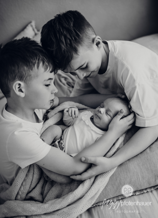 Geschwister halten Baby auf Schoß und kuscheln