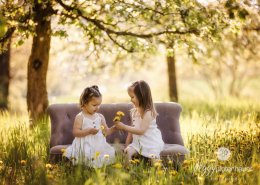 zwei Mädchen sitzen auf Sofa in Frühlingswiese und spielen mit Blumen