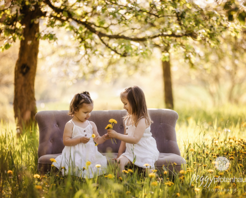 zwei Mädchen sitzen auf Sofa in Frühlingswiese und spielen mit Blumen