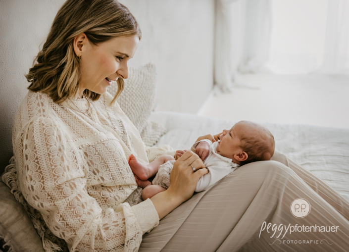 Mama hat Newborn auf Schoss und schaut es glücklich an