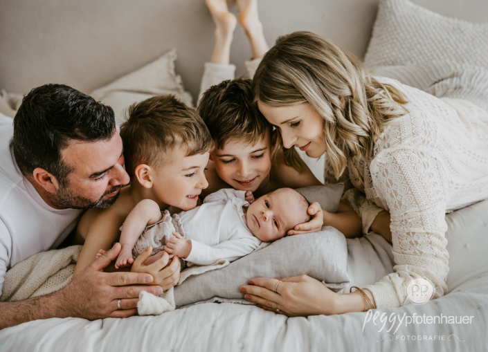 Familie mit drei Kindern liegt auf Bett und kuschelt