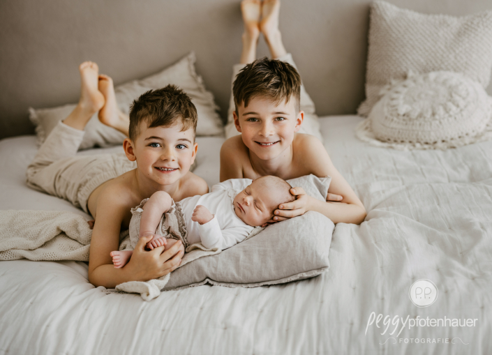 Brüder liegen mit Newborn auf Bett und lachen