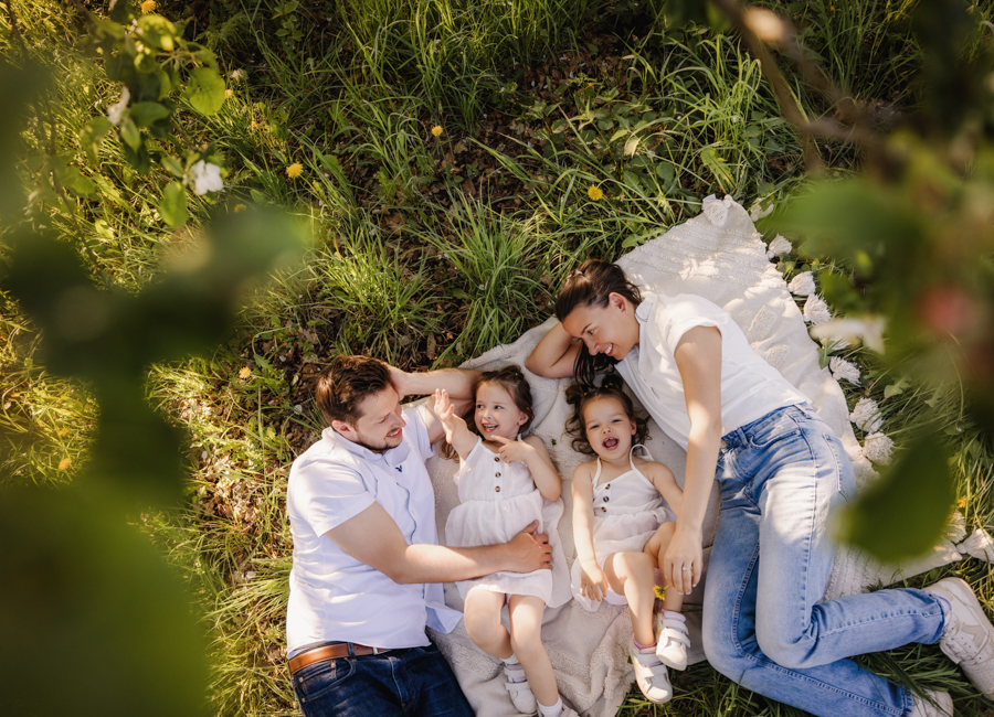 Familienfotos-in-der-Natur-Fuerth Familie liegt auf Decke auf Wiese unter Bäumen und spielt und lacht